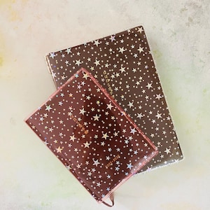 May include: Two brown star-patterned journals with gold foil accents. The smaller journal has the text "2022-2026" and "每日記事手帳" printed on the front. The larger journal has the text "每日記事手帳" printed on the front.