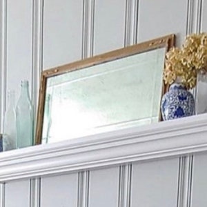 May include: White shelf with a decorative mirror, two clear glass bottles, a blue and white ceramic vase with dried white flowers, and a blue and white ceramic mug.