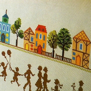 May include: Cross-stitch pattern of a small town with houses, trees, and a family walking down the street. The houses are yellow, red, and brown with white trim. The trees are green. The family is made up of 8 people, all in silhouette.