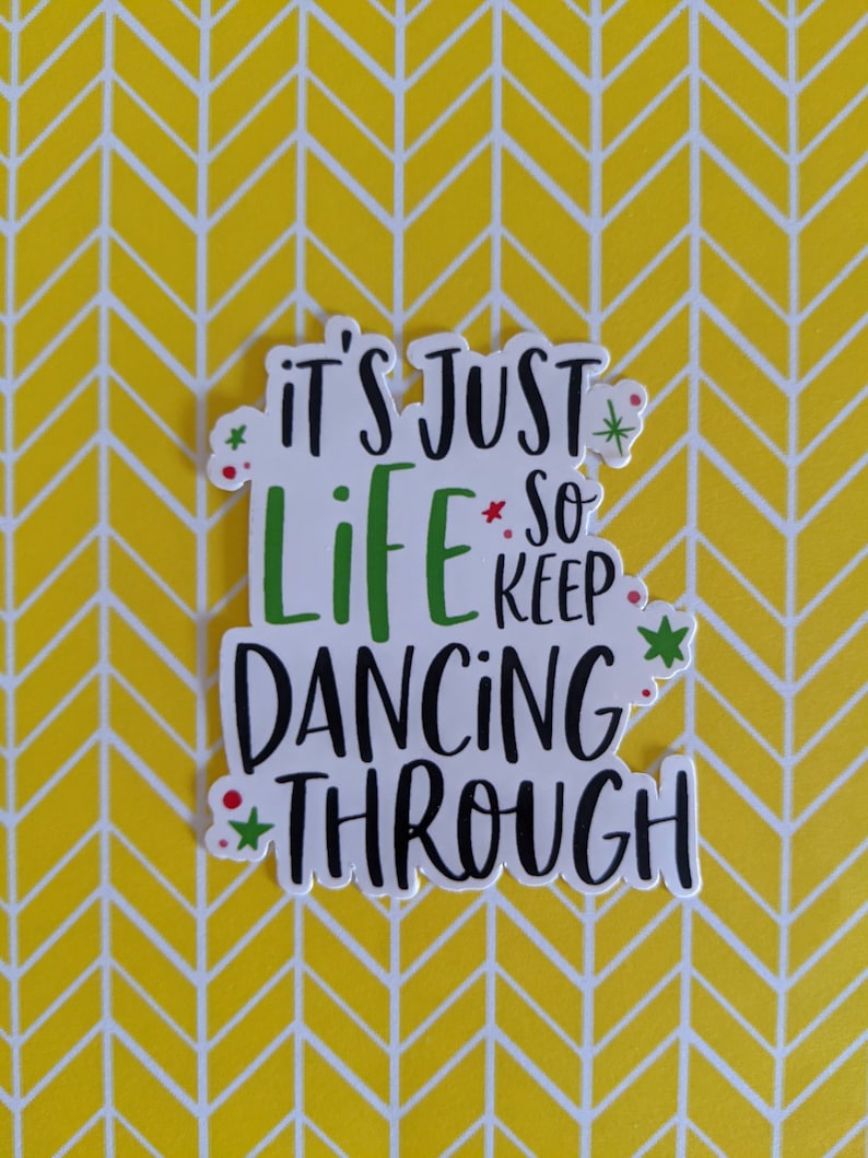 Puede incluir: Una pegatina troquelada con el texto en negro y verde It's Just Life So Keep Dancing Through. El dise&ntilde;o incluye peque&ntilde;os iconos de estrellas verdes y puntos rojos dispersos alrededor de las letras, todo sobre un fondo blanco.