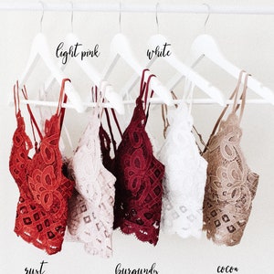 Könnte beinhalten: Fünf Spitzen-Bralettes hängen an weißen Kleiderbügeln. Die Bralettes sind in den Farben Rost, Hellrosa, Burgunderrot, Weiß und Kakao.