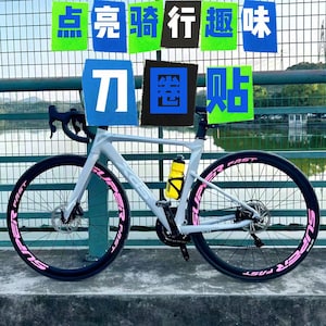 Puede incluir: Una bicicleta de carretera blanca con ruedas negras y letras rosas que dicen "Super Fast" en los neum&aacute;ticos. La bicicleta tiene una botella de agua amarilla unida al cuadro.