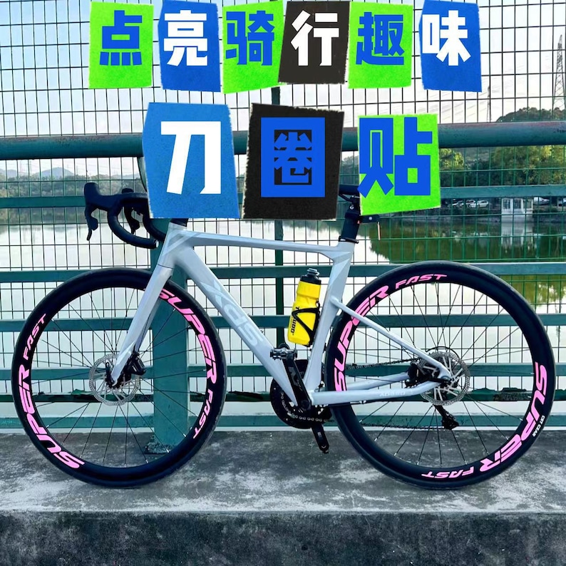 Puede incluir: Una bicicleta de carretera blanca con ruedas negras y letras rosas que dicen "Super Fast" en los neum&aacute;ticos. La bicicleta tiene una botella de agua amarilla unida al cuadro.