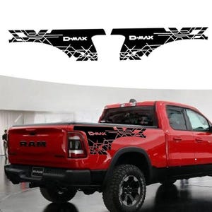May include: Black and white D-MAX truck bed decals with a geometric design. The decals are shown on a red pickup truck. The truck has the word RAM on the tailgate.