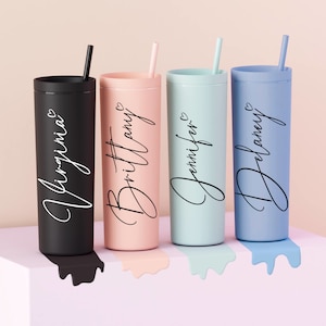 May include: Four personalized tumblers with straws. The tumblers are black, pink, blue, and light blue. Each tumbler has a name written on it in a cursive font: Virginia, Brittany, Jennifer, and Delaney.