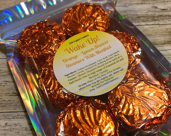 May include: A bag of orange and lemon scented shower steamers with menthol. The bag is labeled "Wake Up! Orange - Lemon Shower Steamers With Menthol".