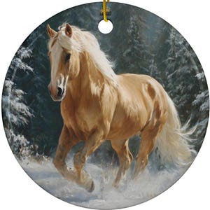 May include: Round ceramic ornament featuring a painting of a golden horse running through snow. The horse has a flowing white mane and tail, set against a backdrop of snow-covered evergreen trees. A gold string is attached for hanging.