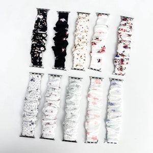 Op de afbeelding: Een verzameling van tien Apple Watch-bandjes met verschillende bloemen- en patroonontwerpen. De bandjes hebben een scrunchie-stijl ontwerp in kleuren als zwart, wit en pasteltinten. Elke band heeft een zilverkleurige connector.