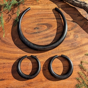 May include: A set of black wooden jewelry, including a large statement necklace and a pair of hoop earrings. The jewelry is displayed on a wooden surface.