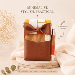 K&ouml;nnte beinhalten: Eine rechteckige Tasche mit einem unteren Teil aus braunem Kunstleder und einem oberen Teil aus wei&szlig;em, gelbem und orangefarbenem Stoff mit Karomuster sowie einer braunen Schleife. Sie enth&auml;lt eine seitliche Stifthalterung mit einem silbernen Stift und den Text MINIMALIST. STYLISH. PRACTICAL.