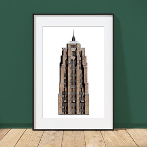 May include: A framed print of a tall, brown brick building with many windows. The building has a spire at the top and is set against a white background. The frame is black, and the print is leaning against a dark green wall on a wooden floor.
