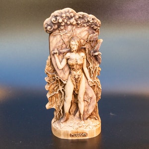 May include: A wooden sculpture of a woman warrior with a sword and shield, standing in front of a tree with lightning bolts. The sculpture is labeled "MORRIGAN".