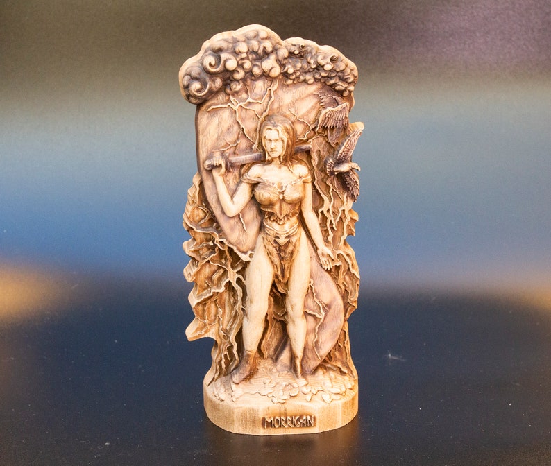 May include: A wooden sculpture of a woman warrior with a sword and shield, standing in front of a tree with lightning bolts. The sculpture is labeled "MORRIGAN".