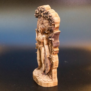 May include: A wooden sculpture of a woman standing in front of a tree. The sculpture is carved in detail and has a natural wood finish.