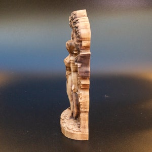 May include: A wooden wall sculpture of a woman standing with her arms raised, carved in a detailed style. The sculpture is made of light brown wood and has a natural finish.