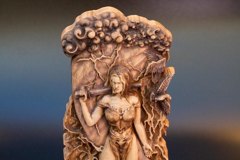 May include: A wooden sculpture of a woman holding a sword, with a background of clouds and birds. The sculpture is carved in a realistic style and has a detailed finish.