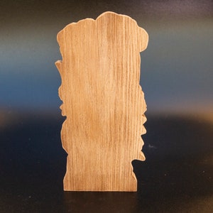 May include: Wooden cutout of a person's face with a detailed design. The cutout is unfinished and has a natural wood color.