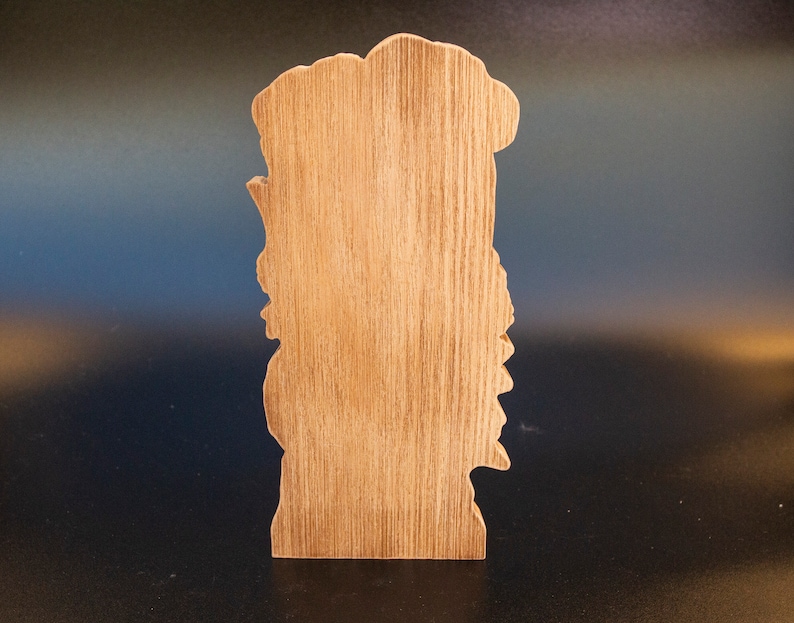 May include: Wooden cutout of a person's face with a detailed design. The cutout is unfinished and has a natural wood color.
