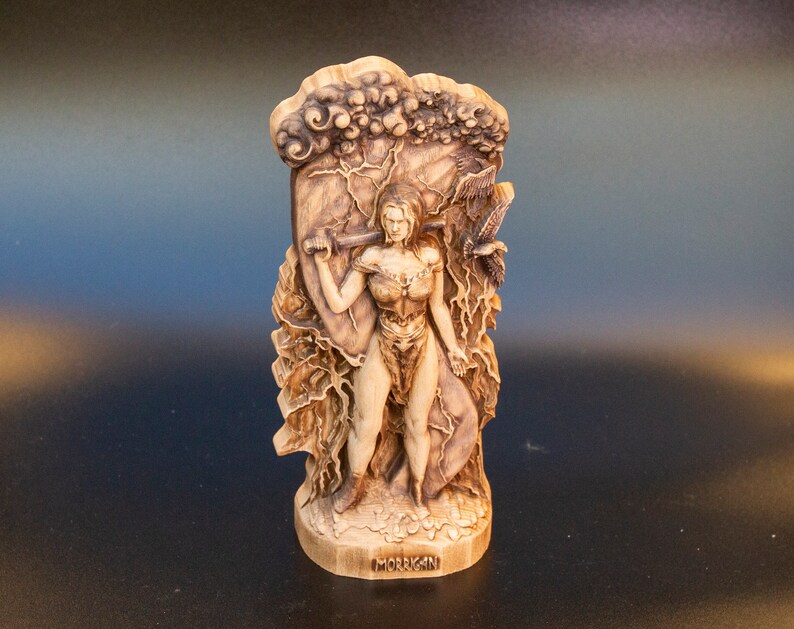 May include: A wooden sculpture of the Celtic goddess Morrigan, depicted as a warrior woman holding a sword and shield. The sculpture is carved with intricate details, including clouds, lightning bolts, and a raven.