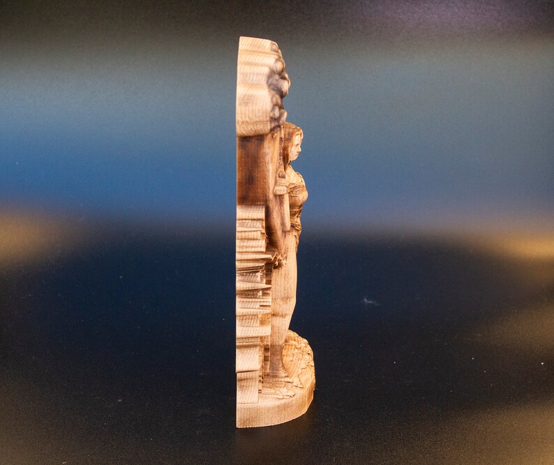 May include: A wooden sculpture of a woman standing with her arms raised, carved in a detailed style. The sculpture is made of light brown wood and has a natural finish.