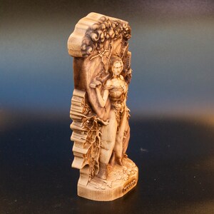May include: A wooden sculpture of a woman standing in front of a tree. The sculpture is carved in detail and has a natural wood finish.