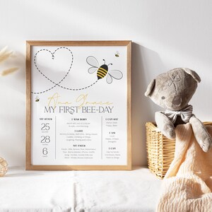 May include: A printable poster with a bee and heart design. The poster is titled "My First Bee-Day" and includes details like the baby's birth stats, favorite things, and abilities. The poster is framed in a light wood frame.