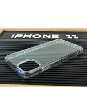 May include: Clear iPhone 11 phone case. The case is transparent and has a sleek design. The words "IPHONE 11" are displayed in white letters on a black background.