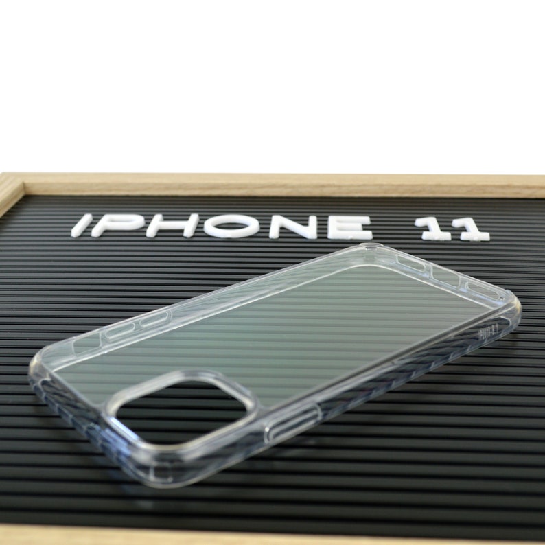 May include: Clear iPhone 11 phone case. The case is transparent and has a sleek design. The words "IPHONE 11" are displayed in white letters on a black background.