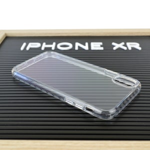 May include: Clear iPhone XR phone case. The transparent case is made of a flexible material and has cutouts for the camera and buttons. The words "IPHONE XR" are displayed in white letters on a black background.