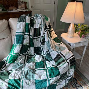 Puede incluir: Una colcha de patchwork verde y blanca, sobre un sofá. La colcha está formada por cuadrados con varios diseños, incluyendo diseños florales, a rayas y de lunares. La colcha parece estar hecha a mano y está hecha de tela suave.
