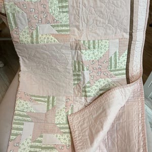 May include: A pink and white patchwork quilt with a variety of patterns, including stripes, checks, and a repeating horse motif. The quilt has a brown border and is folded over, revealing a quilted interior.