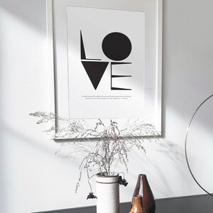 May include: A black and white framed print with the word "LOVE" in bold, geometric shapes. The print includes a quote about love. The print is displayed on a black table with a vase of dried flowers and two decorative vases.