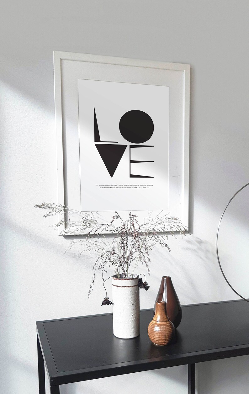 May include: A black and white framed print with the word "LOVE" in bold, geometric shapes. The print includes a quote about love. The print is displayed on a black table with a vase of dried flowers and two decorative vases.