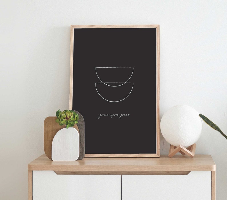 Puede incluir: Una impresi&oacute;n enmarcada en negro con un dise&ntilde;o minimalista de dos semic&iacute;rculos superpuestos en blanco. El texto "grace upon grace" est&aacute; escrito debajo del dise&ntilde;o.