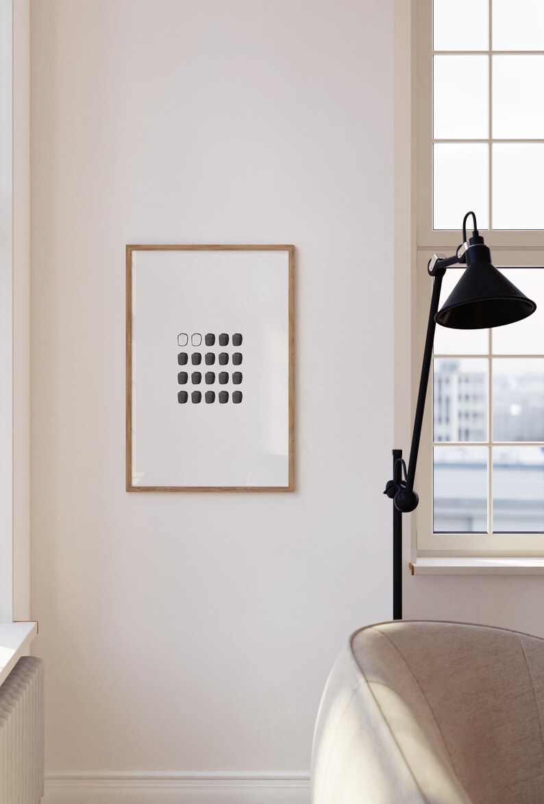 May include: A framed black and white print of a geometric design with a series of squares in varying shades of gray. The print is hanging on a white wall in a modern interior.