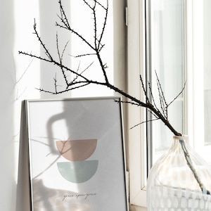 K&ouml;nnte beinhalten: Ein gerahmter Druck mit einem minimalistischen Design aus zwei sich &uuml;berlappenden Halbkreisen in Rosa- und Blaut&ouml;nen. Der Druck enth&auml;lt den Text "grace upon grace" in einer kursivschriftlichen Schriftart.