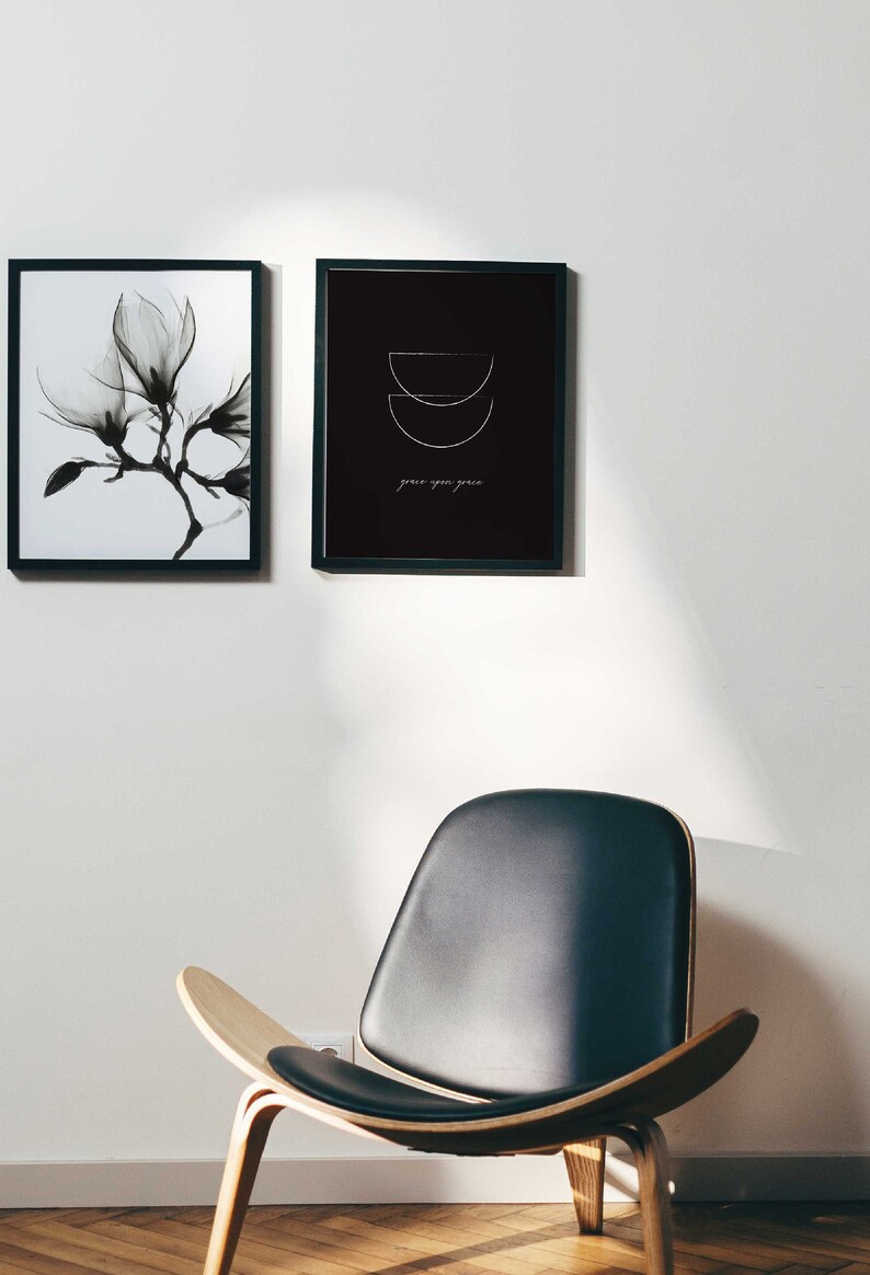 Puede incluir: Dos impresiones en blanco y negro enmarcadas en una pared blanca. La impresi&oacute;n de la izquierda presenta una imagen en blanco y negro de una flor de magnolia. La impresi&oacute;n de la derecha presenta un fondo negro con un dise&ntilde;o geom&eacute;trico blanco y el texto "grace upon grace". Una silla de cuero negro con patas de madera se encuentra frente a la pared.