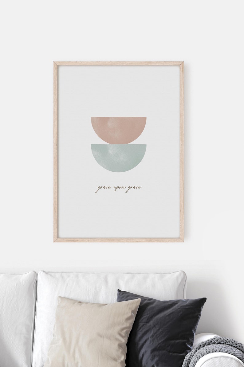 K&ouml;nnte beinhalten: Ein gerahmter Druck mit einem minimalistischen Design, das zwei sich &uuml;berlappende Halbkreise in gedeckten Rosa- und Blaut&ouml;nen zeigt. Der Text "grace upon grace" ist in einer kursivschriftlichen Schriftart unter den Formen geschrieben.