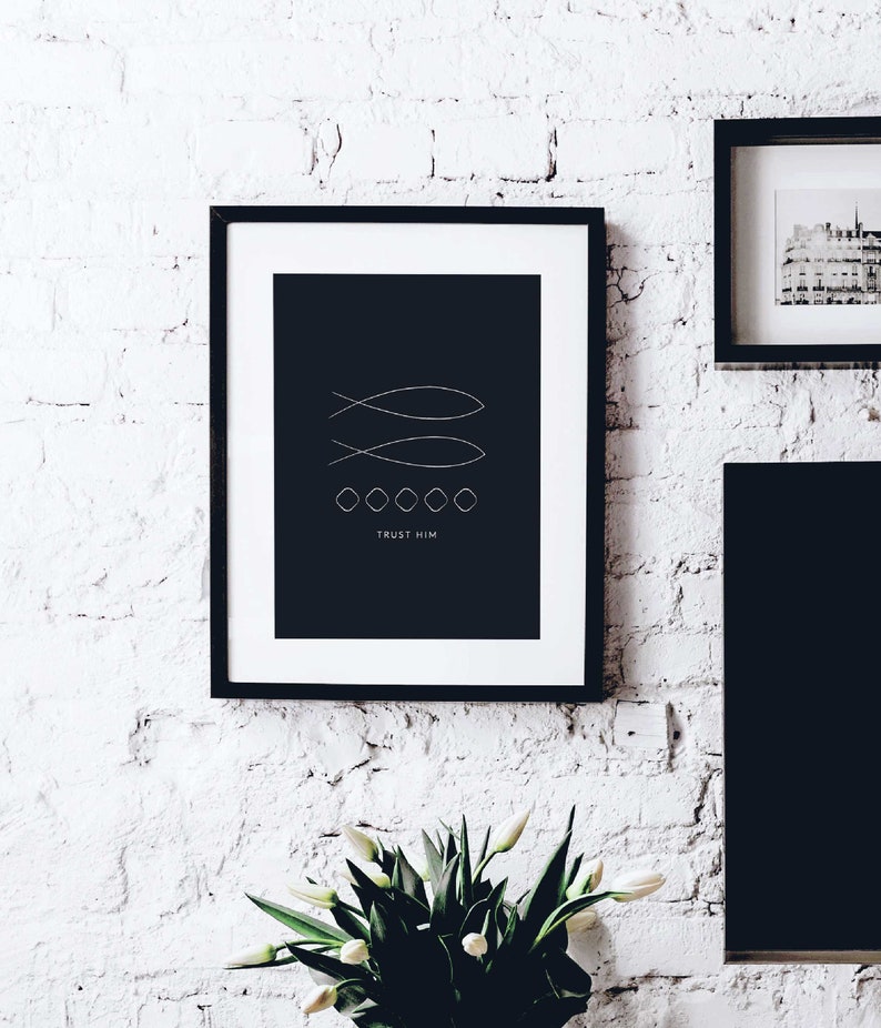 May include: Black and white minimalist print with two stylized fish and the text "TRUST HIM" in a black frame on a white brick wall.