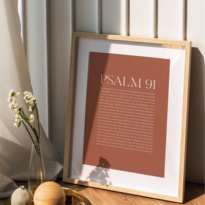 May include: A framed print with a brown background and white text. The text reads "Psalm 91" and includes a passage from the Bible. The print is sitting on a wooden surface with a gold tray and decorative objects.