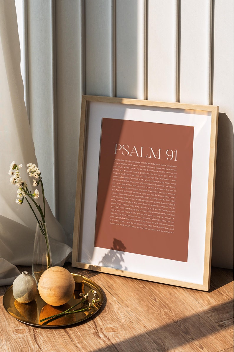 May include: A framed print with a brown background and white text. The text reads "Psalm 91" and includes a passage from the Bible. The print is sitting on a wooden surface with a gold tray and decorative objects.