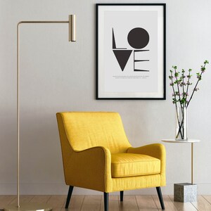 May include: A yellow armchair with black legs sits in a room with a floor lamp and a framed print of the word "LOVE" in black and white geometric shapes.