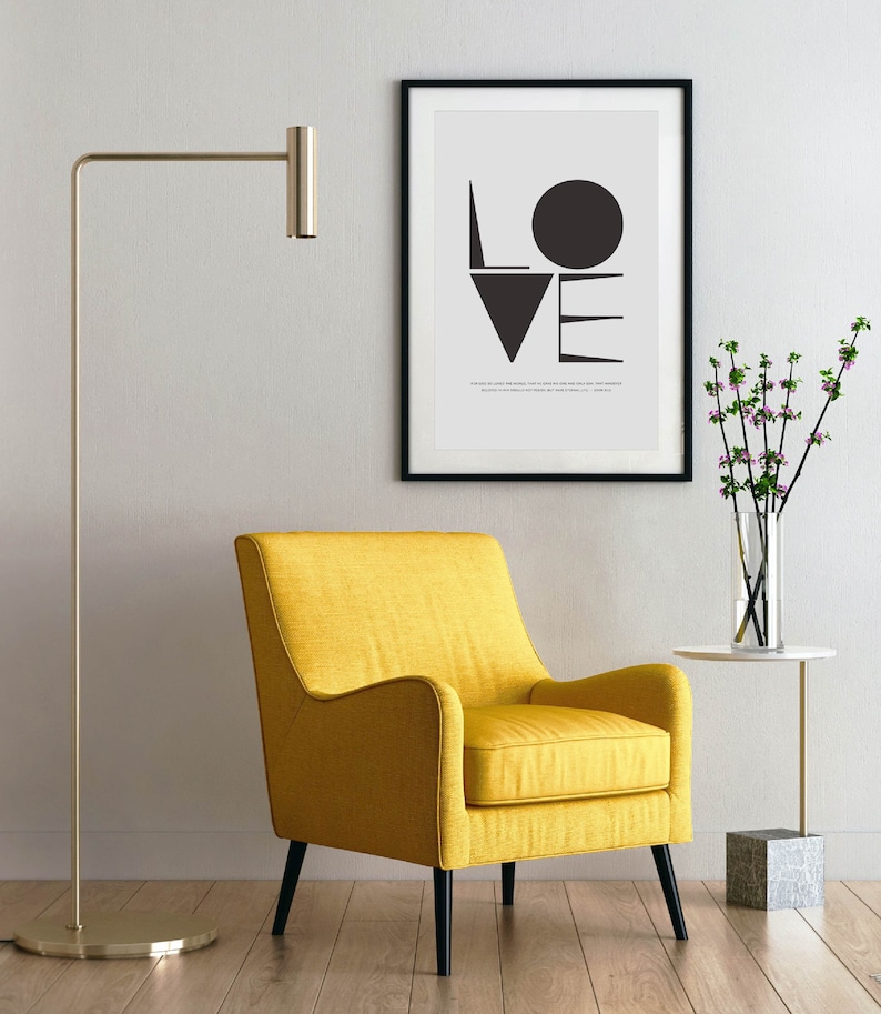 May include: A yellow armchair with black legs sits in a room with a floor lamp and a framed print of the word "LOVE" in black and white geometric shapes.