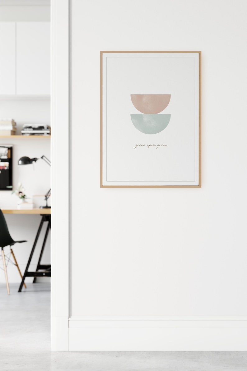 K&ouml;nnte beinhalten: Ein gerahmter Druck mit einem minimalistischen Design, das zwei sich &uuml;berlappende Halbkreise in Rosa- und Blaut&ouml;nen zeigt. Der Text "grace upon grace" ist darunter in Kursivschrift geschrieben.