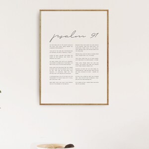 May include: A framed print of Psalm 91, a passage from the Bible, with a white background and black text. The text is centered on the page and is surrounded by a thin black border.