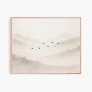 Pode incluir: Uma impressão em aquarela emoldurada retratando uma paisagem serena de montanhas em camadas em tons de bege e cinza suaves. Pássaros silhuetados voam pelo céu. A obra de arte é emoldurada em uma moldura de madeira marrom clara, criando uma estética calma.