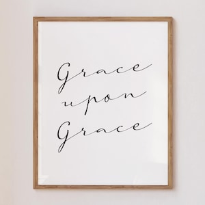 Puede incluir: Impresión enmarcada con las palabras "Grace upon Grace" en elegante escritura negra. El texto está centrado sobre un fondo blanco, dentro de un marco de madera marrón claro, adecuado para la decoración del hogar.