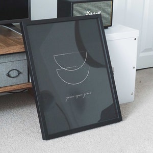 Puede incluir: Impresi&oacute;n enmarcada en negro con un dise&ntilde;o minimalista de dos semic&iacute;rculos superpuestos en blanco. El texto "grace upon grace" est&aacute; escrito en blanco debajo del dise&ntilde;o.