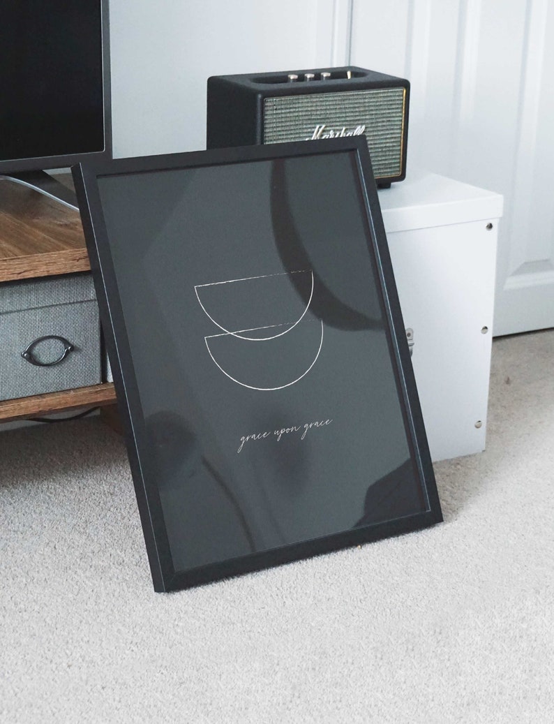 Puede incluir: Impresi&oacute;n enmarcada en negro con un dise&ntilde;o minimalista de dos semic&iacute;rculos superpuestos en blanco. El texto "grace upon grace" est&aacute; escrito en blanco debajo del dise&ntilde;o.
