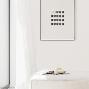 May include: A white, rectangular ottoman with a magazine and a small bowl of green grapes on top. A framed black and white print of a geometric pattern hangs on the wall behind the ottoman.